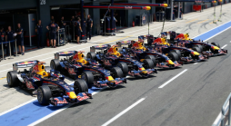 Eine Reihe von Red Bull Formel-1-Rennwagen steht aufgereiht vor der Boxengasse, bereit für das Rennen.