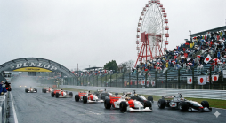 Formel-Rennwagen auf nasser Rennstrecke vor dem Start, mit Dunlop-Bogen, Riesenrad und Zuschauern unter Regenschirmen in Japan.
