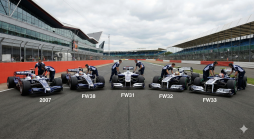 Fünf Williams F1-Boliden der Jahre 2007, FW38, FW31, FW32 und FW33 auf einer Rennstrecke mit Crew-Mitgliedern und Tribünen im Hintergrund.