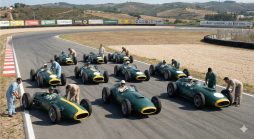 Mehrere klassische grüne Rennwagen mit Fahrern und Mechanikern auf der Start-/Zielgeraden des Autódromo do Estoril, bereit für ein historisches Rennen.
