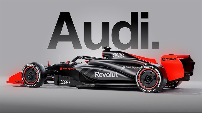 Schwarzer und roter Audi Formel 1 Rennwagen im Seitenprofil, mit dem großen 'Audi.' Logo im Hintergrund auf grauem Untergrund.